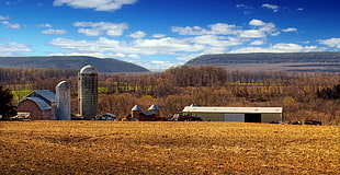 white cumulus clouds over ranch with barn and silos during daytime