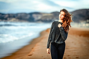 woman in gray sweater standing near shoreline during daytime HD wallpaper