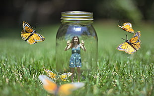 selective focus photography of a woman in a jar surrounded by butterflies on grass