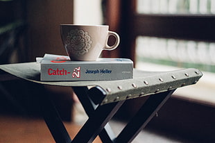 selective focus photography of white ceramic mug on top of Catch 22 by Joseph Heller book