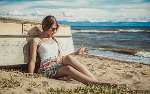 woman in white spaghetti strap top sitting on sand beach