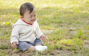 baby wearing white zip-up hooded jacket and blue shorts sitting on grass