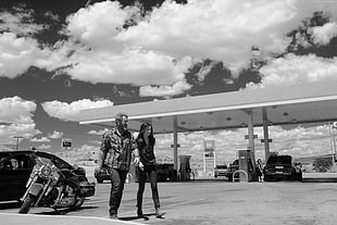 grayscale photo of man and woman near gasoline station
