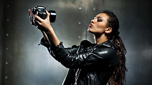 woman in black leather top taking photo of self using SLR camera