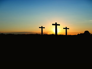 silhouette photo pf three cross during golden hour