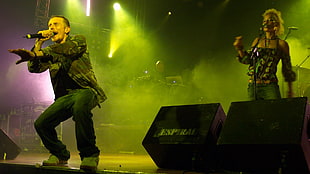 man in camouflage jacket holding microphone bend his knees in stage whiel sinning