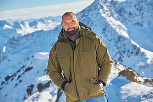 man wearing green zip-up jacket near snow-capped mountain photo taken during daytime HD wallpaper