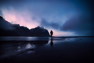 silhouette of man standing on sea during night time