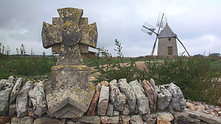 gray concrete cross with rocks near grass and windmill