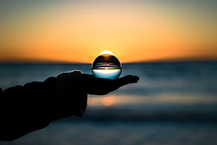 crystal ball on person's hand during yellow sunset