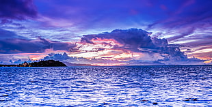 body of water under cloudy skies during sunset