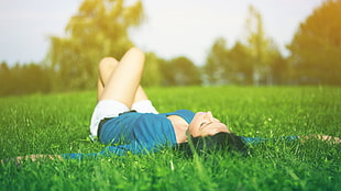 woman wearing blue top and white bottoms leaning on green grass