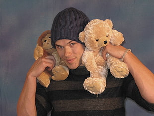 person in knit cap holding two bear plush toys