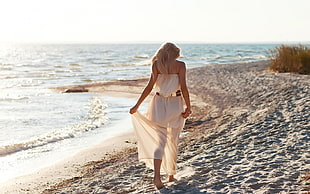 woman wearing white tube maxi dress walking near seashore during daytime HD wallpaper