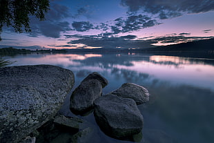 boulders on body of water surrounded by trees under stratus clouds