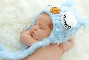 baby with blue and white critter cap on white textile