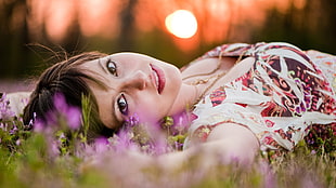 woman wearing white and brown floral scoop-neck top lying on green grass during daytime