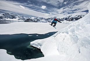 photography of person snowboarding on snow coated ground near body of water during daytime