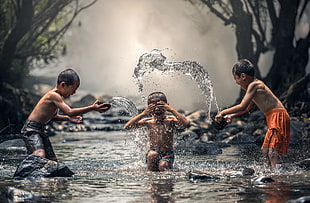three children playing on river during day time