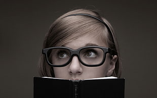 grayscale photo of woman wearing eyeglasses while holding a book