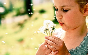 girl wearing green top blowing white dandelion flowers