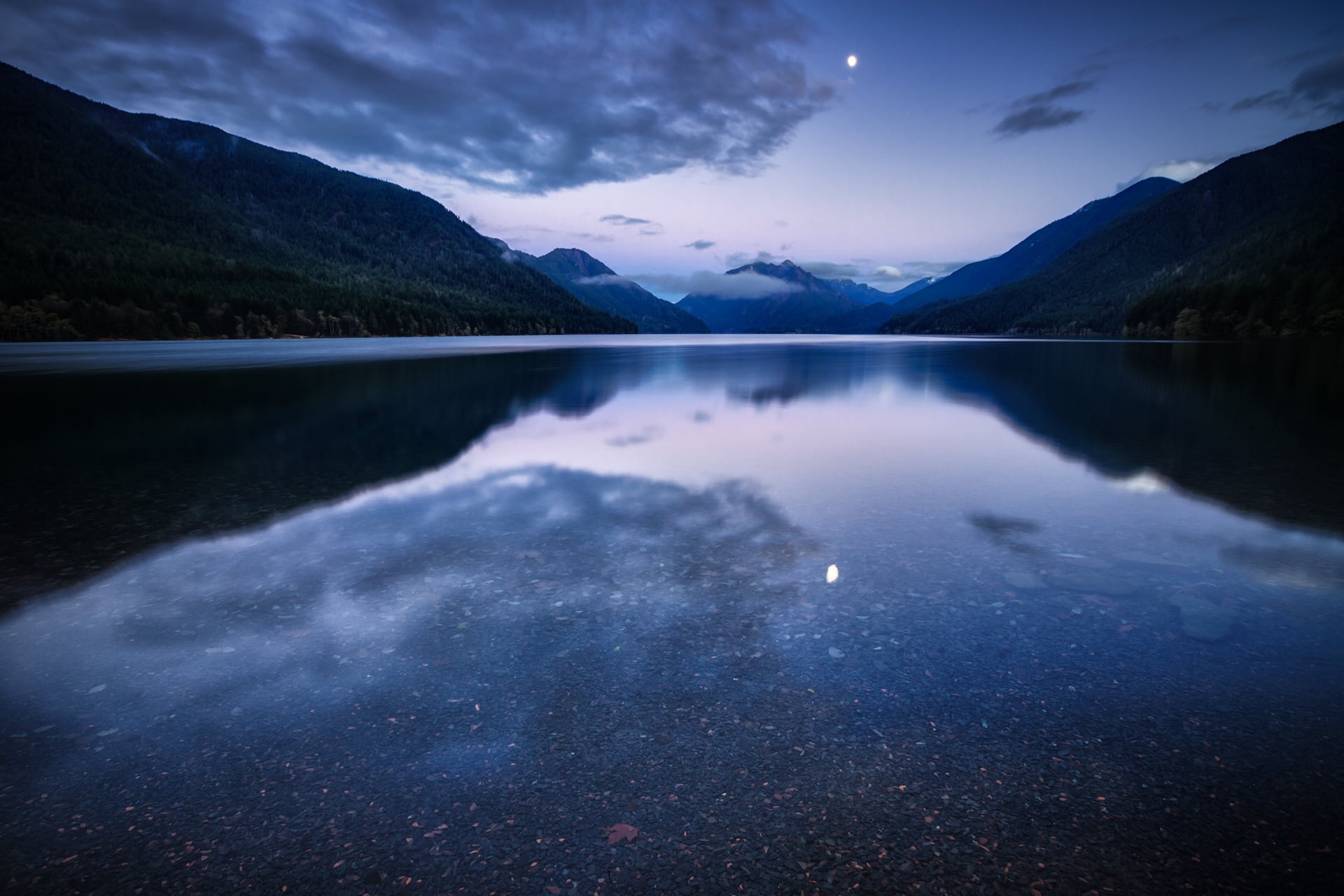 body of water between green mountains under gray cloudy sky