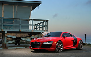 red Audi R7 parked beside blue wooden house