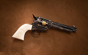 black revolver with white handle on brown surface