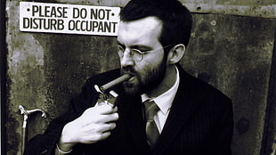 grayscale photo of man in suit smoking cigar and holding flip lighter