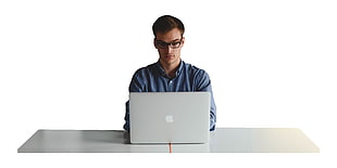 man wearing blue buttoned long-sleeved top and black eyeglasses using MacBook