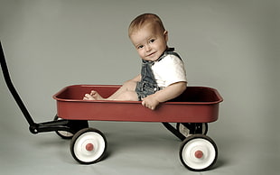 baby on red and black toy wagon