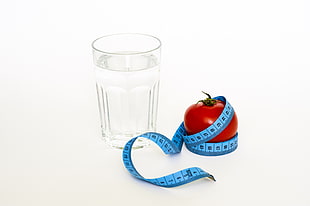 blue tape measure on tomato with clear water glass