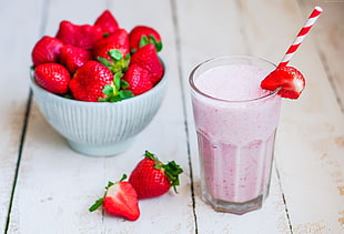 Strawberry smoothies on clear high-ball glass beside strawberries on white ceramic bowl