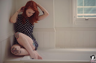 photo of woman wearing black and white floral top sitting on white ceramic bath tub
