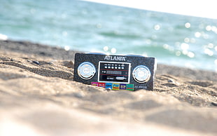 shallow focus photography of black Atlanta radio on white sand beach during daytime
