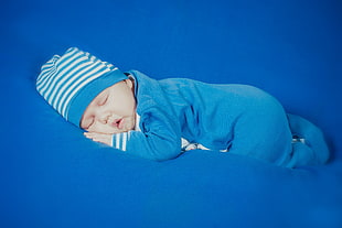 baby in blue footie pajama and white and blue stripe knit cap sleeping on blue cushion HD wallpaper
