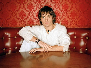 man wearing white long-sleeved shirt sitting on brown leather padded sofa