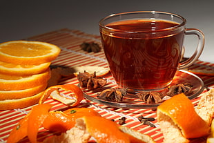 clear glass teacup with red beverage near sliced orange fruit on table