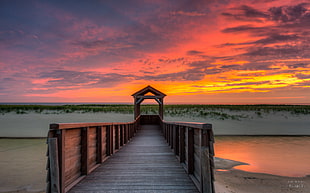 brown wooden pathway near body of water during sunset