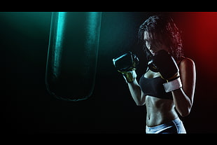 woman in black sports bra wearing pair of black boxing gloves in front of black heavy bag
