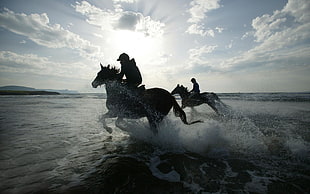 silhouette of two person ride on horse under cloudy sky