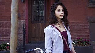 woman wearing maroon shirt and white jacket standing near building