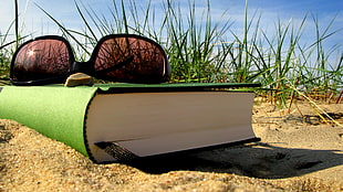 black framed sunglasses on green hardbound book on sand