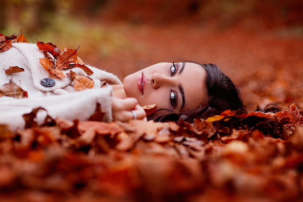 woman in white pea coat wearing ring laying on dried leaves HD wallpaper