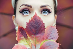 woman with makeup on her face and brown leaf covering her nose and mouth