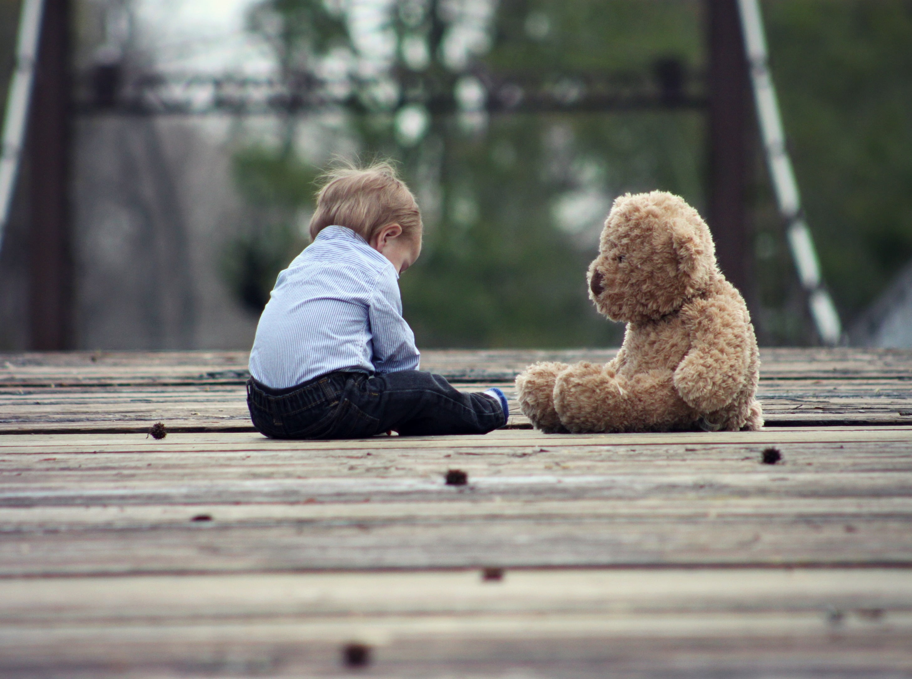 children sitting beside of brown bear plush toy