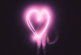 photo of woman making heart sign with pink light in dark room