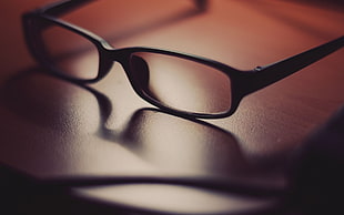 rectangular black plastic-framed eyeglasses on wooden surface
