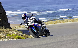 photo of man riding a white and blue sports bike during daytime