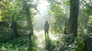 man in brown and white plaid shirt standing between green trees